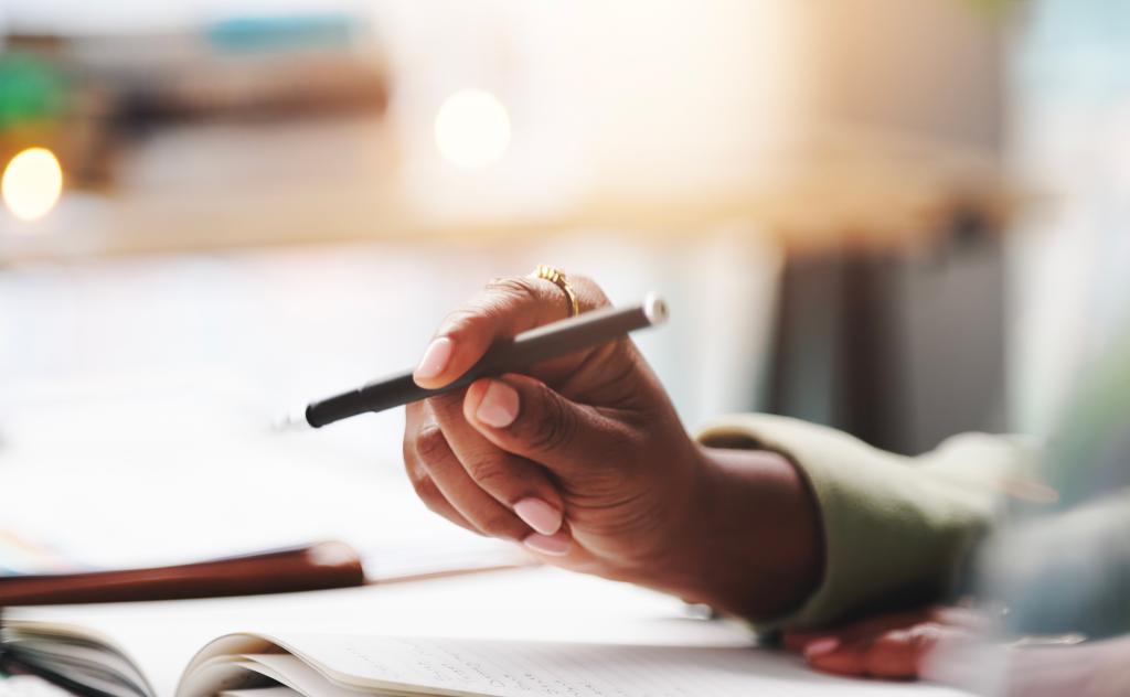 Closeup of hand holding pen, sitting on desk with diary